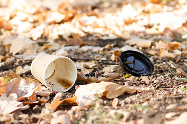 Paper coffee cup with plastic lid on the ground. Discarded disposable coffee cup with a plastic lid. Empty single use paper coffee cup