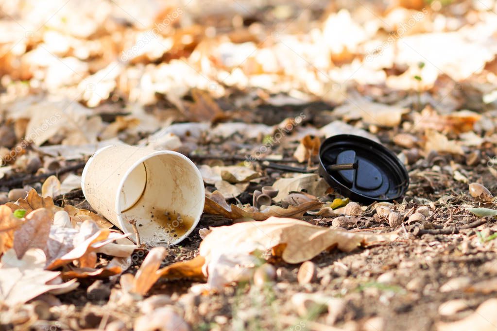 Paper coffee cup with plastic lid on the ground. Discarded disposable coffee cup with a plastic lid. Empty single use paper coffee cup