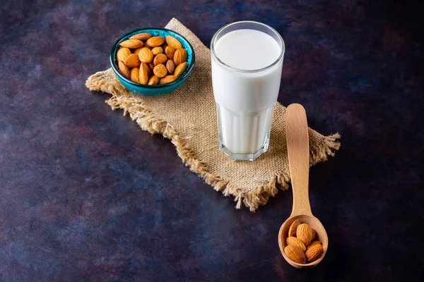 Almond milk with almond on dark background. Homemade organic almond milk in a glass for healthy breakfast. Vegan milk from almonds nuts on a sackcloth. Alternative milk. Top view. Copy space