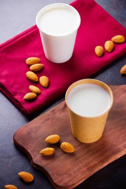 Badem sütü ve koyu arkaplan. Tahta bir tahtanın üzerinde kağıt bardakta ev yapımı organik badem sütü. Kraft kağıt bardakta bademli fındıklı vejetaryen sütü. Alternatif süt. Sıfır atık