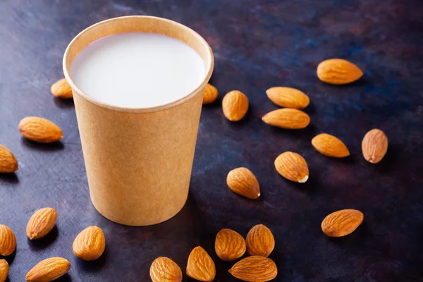 Almond milk with almond on dark background. Homemade organic almond milk in a paper cup for healthy breakfast. Vegan milk from almonds nuts in kraft paper cup. Alternative milk. Zero waste