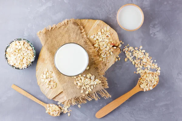 Oat milk. Organic oat milk on a wooden stand. Vegan non-dairy organic drink with oat flakes. Alternative milk on cement background. Zero waste