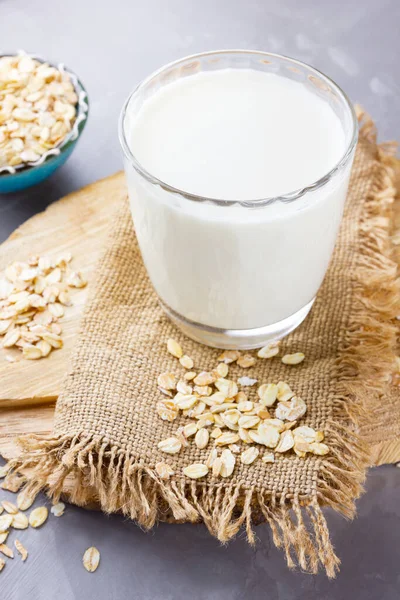 Oat milk. Organic oat milk on a wooden stand. Vegan non-dairy organic drink with oat flakes. Alternative milk on cement background. Zero waste