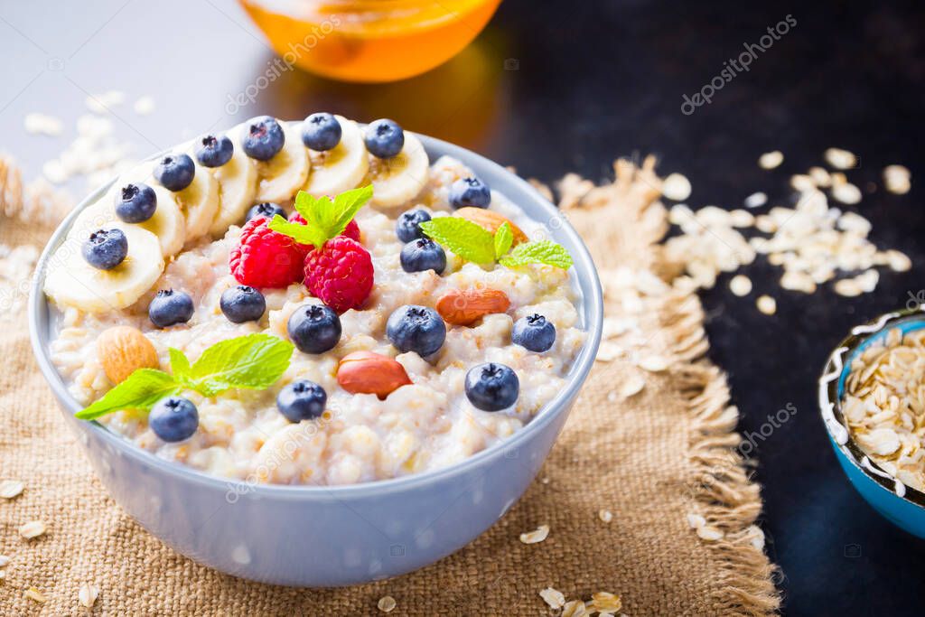 Healthy breakfast. Oatmeal porridge with berries, fruits and honey on dark background. Oatmeal with raspberries, blueberries and almonds on sackcloth. Top view