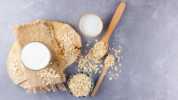 Oat milk. Organic oat milk on a wooden stand. Vegan non-dairy organic drink with oat flakes. Alternative milk on cement background. Zero waste