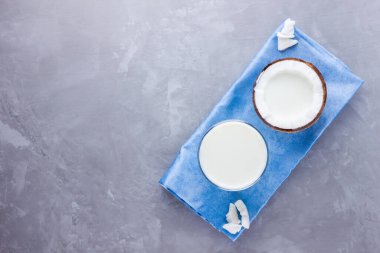 Hindistan cevizi sütü ve gri arka planda camlı hindistan cevizi. Mavi peçetede hindistan cevizi vejetaryen sütü. Sağlıklı içki konsepti. Minimalizm. Alternatif süt. Boşluğu kopyala