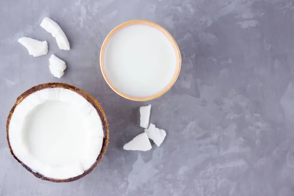 Coconut milk and coconut in paper glass on gray background. Coconut vegan milk non dairy on cement. Healthy drink concept. Alternative milk. Top view