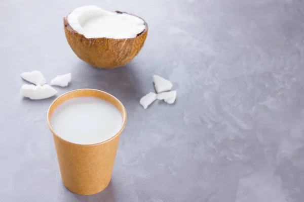 Coconut milk and coconut in paper glass on gray background. Coconut vegan milk non dairy on cement. Healthy drink concept. Alternative milk. Top view