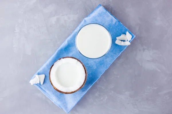 Coconut milk and coconut in glass on gray background. Coconut vegan milk non dairy on blue napkin. Healthy drink concept. Minimalism. Alternative milk. Copy space