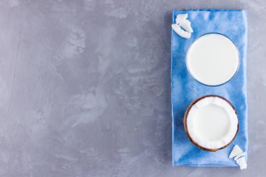 Hindistan cevizi sütü ve gri arka planda camlı hindistan cevizi. Mavi peçetede hindistan cevizi vejetaryen sütü. Sağlıklı içki konsepti. Minimalizm. Alternatif süt. Boşluğu kopyala