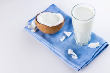 Beyaz arka planda hindistan cevizi sütü ve bardakta hindistan cevizi. Mavi peçetede hindistan cevizi vejetaryen sütü. Sağlıklı içki konsepti. Minimalizm. Alternatif süt. Boşluğu kopyala