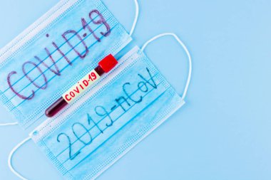 Coronavirus - COVID-19. Mavi arka planda COVID-19 koronavirüsünden alınan kanla test tüpü. Koruyucu tıbbi maske ve test tüpü. Boşluğu kopyala