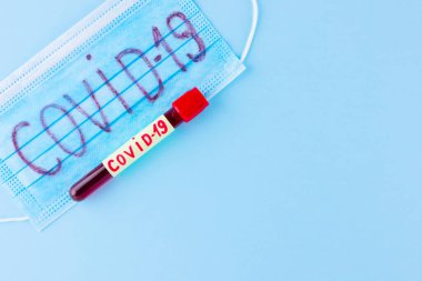 Coronavirus - COVID-19. Mavi arka planda COVID-19 koronavirüsünden alınan kanla test tüpü. Koruyucu tıbbi maske ve test tüpü. Boşluğu kopyala