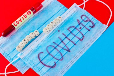 Coronavirus - COVID-19. Kırmızı arka planda COVID-19 tarafından tanımlanmış kan olan test tüpü. Koruyucu tıbbi maske ve test tüpü. Tahta küplerden yapılmış 