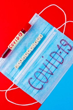 Coronavirus - COVID-19. Kırmızı arka planda COVID-19 tarafından tanımlanmış kan olan test tüpü. Tıbbi maske ve test tüpü. Tahta küplerden yapılmış 