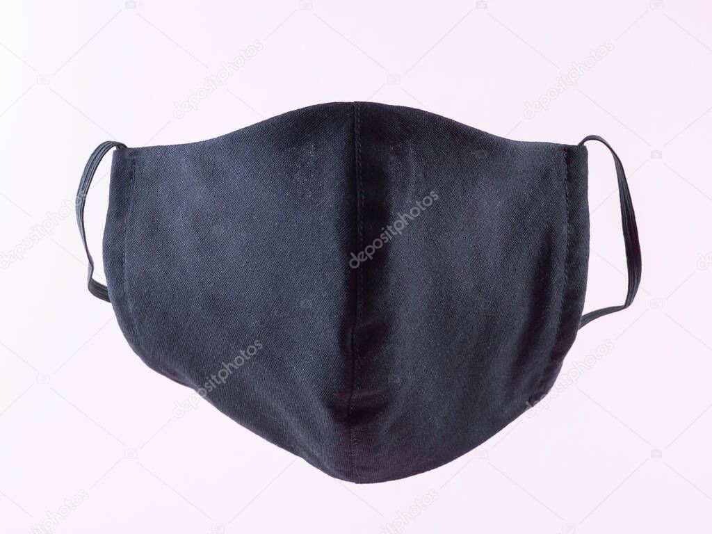 Handmade protective mask. Antivirus mask made from cotton. Black stylish face mask during a pandemic virus COVID-19. Face protective mask on a pink background