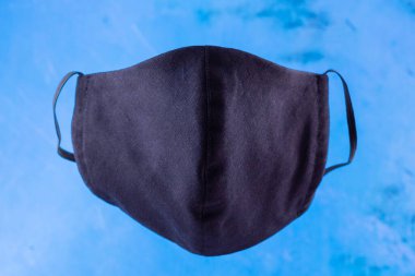 El yapımı koruyucu maske. Pamuktan yapılmış antivirüs maskesi. Salgın bir virüs olan COVID-19 sırasında siyah stil bir yüz maskesi. Mavi arka planda yüz koruyucu maskesi