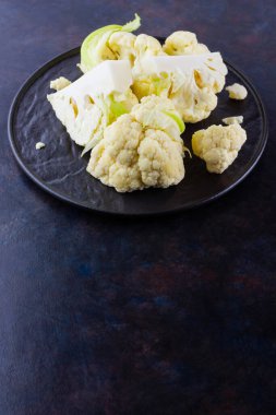 Siyah bir tabakta karnabahar. Karanlık bir arka planda dilimlenmiş taze karnabahar. Tabakta organik lahana dilimleri. Üst Manzara. Boşluğu kopyala