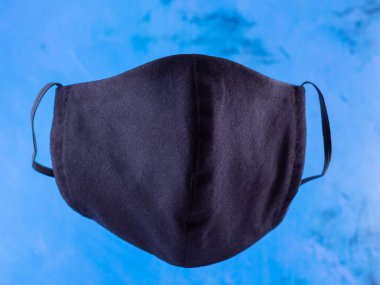Koruyucu maske. Pamuktan yapılmış antivirüs maskesi. Salgın bir virüs olan COVID-19 sırasında siyah yüz maskesi. Mavi arka planda yüz koruyucu maskesi