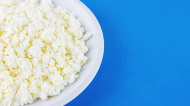 Mavi arka planda beyaz tabakta süzme peynir. Organik ekolojik sağlıklı yemek, süt ürünleri. Bir tabak ev yapımı süzme peynir. Üst Manzara. Boşluğu kopyala