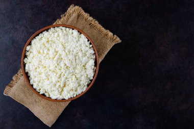 Çuval bezinde süzme peynir. Koyu bir arka planda taze süzme peynir. Siyah arka planda yumuşak peynir. Minimalizm. Üst Manzara. Boşluğu kopyala