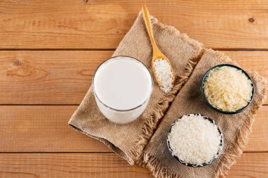 Tahta tahtalarda pirinç ve süt tohumu. Çuval bezinde pirinç sütü. Ahşap arka planda süt içermeyen vejetaryen süt. Yükselişten gelen alternatif süt. Kırsal tarzda. Üst görünüm