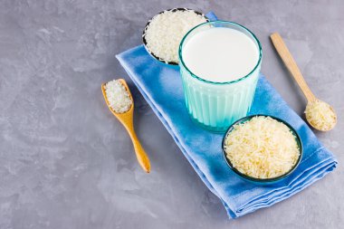 Gri arka planda pirinç ve süt tohumu. Mavi bir peçetede pirinç sütü. Çimento arka planında süt içermeyen vegan. Yükselişten gelen alternatif süt. Minimalizm. Boşluğu kopyala