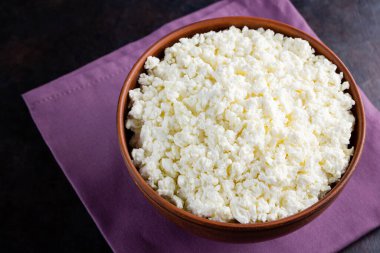 Koyu bir arka planda süzme peynir. Kâsede taze süzme peynir. Keten peçetede yumuşak peynirli kil tabağı. Minimalizm. Üst Manzara. Boşluğu kopyala