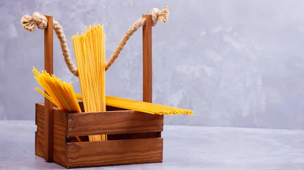 Pasta in a wooden box. Donation wooden box with raw spaghetti on a gray background. Social assistance with food. Safe food delivery. Food donation concept. Copy space