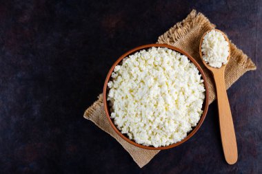 Çuval bezinde süzme peynir. Koyu arkaplanda taze süzme peynir ve ahşap kaşık. Siyah arka planda yumuşak peynir. Üst Manzara. Boşluğu kopyala