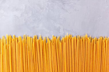 Gri arka planda sarı makarna. Çimento arka planında spagetti. Çiğ spagetti bolonez. Yemek geçmişi konsepti. Üst görünüm