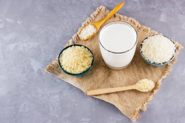 Gri arka planda pirinç ve süt tohumu. Çuval bezinde pirinç sütü. Çimento arka planında süt içermeyen vegan. Yükselişten gelen alternatif süt. Kırsal tarzda. Boşluğu kopyala