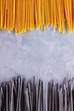 Gri arka planda siyah ve sarı makarna. Çimento arka planında sarı ve siyah spagetti. Çiğ spagetti bolonez. Yemek geçmişi konsepti. Üst görünüm