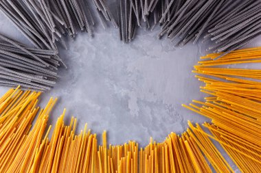 Gri arka planda siyah ve sarı makarna. Çimento arka planında sarı ve siyah spagetti. Çiğ spagetti bolonez. Yemek geçmişi konsepti. Üst görünüm