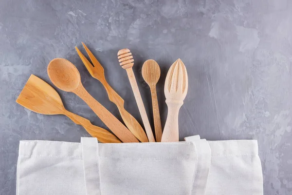 Zero waste concept. Cotton eco bag and wooden cutlery on gray background. Set of Eco friendly wooden cutlery. Plastic free concept. Minimalism. Top view. Copy space