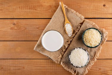 Tahta tahtalarda pirinç ve süt tohumu. Çuval bezinde pirinç sütü. Ahşap arka planda süt içermeyen vejetaryen süt. Yükselişten gelen alternatif süt. Kırsal tarzda. Üst görünüm