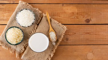Tahta tahtalarda pirinç ve süt tohumu. Çuval bezinde pirinç sütü. Ahşap arka planda süt içermeyen vejetaryen süt. Yükselişten gelen alternatif süt. Kırsal tarzda. Üst görünüm