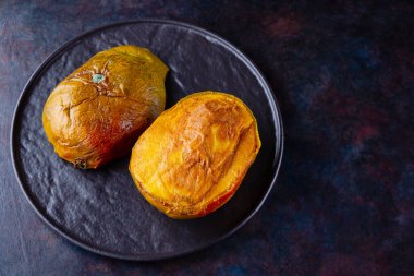 Çirkin mango. Karanlık arka planda bozulmuş mango. Siyah tabakta çürük mango. Üst Manzara. Boşluğu kopyala