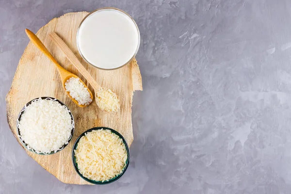 Gri arka planda pirinç ve süt tohumu. Tahta tezgahta cam içinde pirinç sütü. Çimento arka planında süt içermeyen vegan. Yükselişten gelen alternatif süt. Boşluğu kopyala
