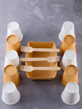 Sıfır kayıp. Tek kullanımlık sofra takımı. Gri arka planda bambu ahşap ve kağıttan yapılmış çevre dostu tek kullanımlık aletler. Kağıt bardaklar, fast food kapları ve bambu ahşap çatal bıçaklar.