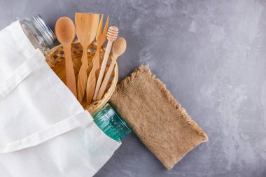 Sıfır atık. Eko çanta, cam ve gri arka planda ahşap çatal bıçak. Çevre dostu ahşap çatal bıçak takımı, çuval bezi ve mason kavanozu. Plastiksiz konsept. Üst Manzara. Boşluğu kopyala