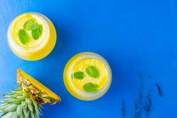 Pineapple juice on a blue background. Juice for detox in the glass. Pineapple smoothie with fresh pineapple. Summer drink with mint. Top view. Copy space