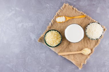 Gri arka planda pirinç ve süt tohumu. Çuval bezinde pirinç sütü. Çimento arka planında süt içermeyen vegan. Yükselişten gelen alternatif süt. Kırsal tarzda. Boşluğu kopyala