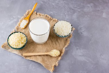 Gri arka planda pirinç ve süt tohumu. Çuval bezinde pirinç sütü. Çimento arka planında süt içermeyen vegan. Yükselişten gelen alternatif süt. Kırsal tarzda. Boşluğu kopyala