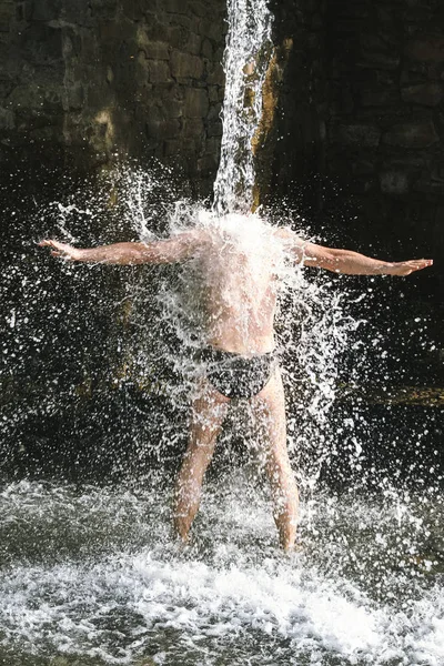 a man stands under a large stream of water under a waterfall