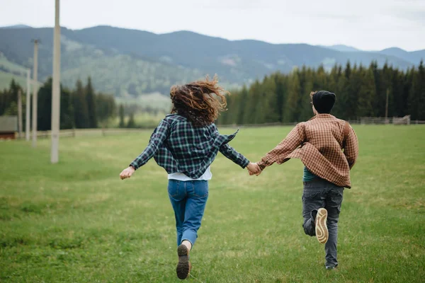 Un par de amantes tomados de la mano y huyendo en las montañas. Mujer y hombre enamorados caminando al aire libre . — Foto de Stock