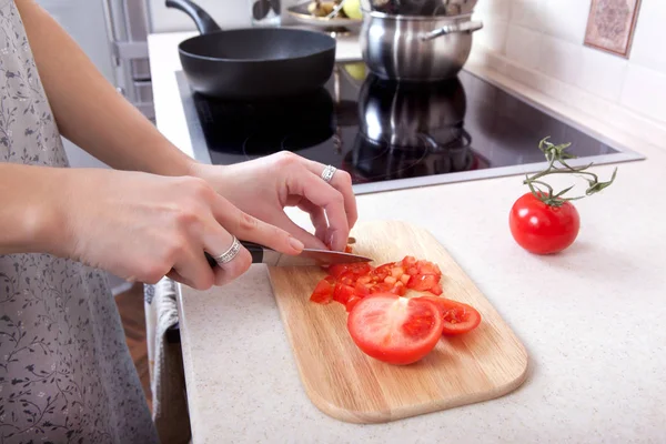 Mulher corta tomates com uma faca na mesa da cozinha . — Fotografia de Stock