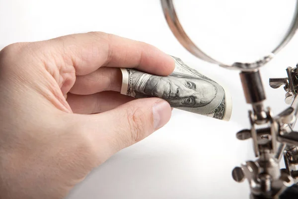 Finance inspector. Checks money for authenticity through a magnifying glass. Hands close-up. — Stock Photo, Image
