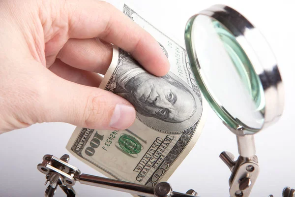 Finance inspector. Checks money for authenticity through a magnifying glass. — Stock Photo, Image