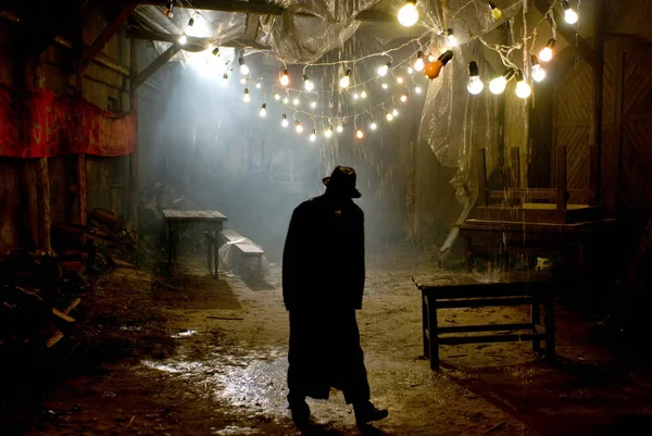 Homme au chapeau noir sous la pluie dans la rue sombre et couverte — Photo